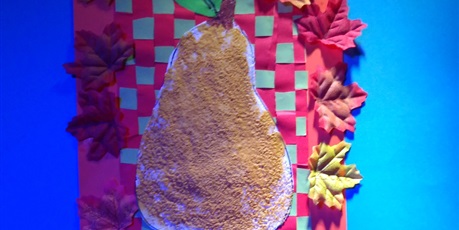 Powiększ grafikę: Praca konkursowa Klaudii - żółta gruszka malowana na cukrze, umieszczona na przeplatance czerwono-zielonej, całość otoczona sztucznymi liśćmi.